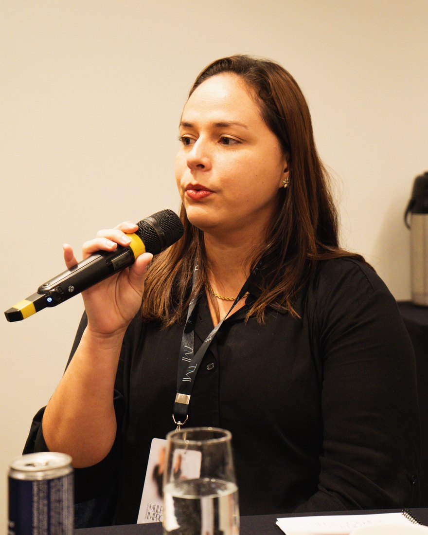 Valéria Moura falando ao microfone durante um evento profissional